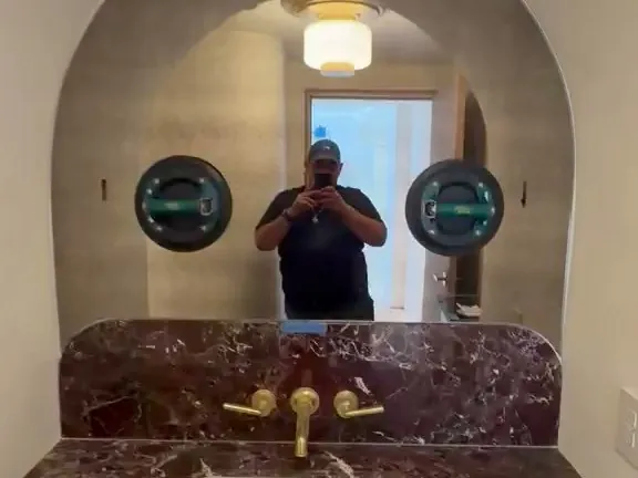 Arched antique-finish vanity mirror being finish-checked during installation over a red marble counter with brass fixtures in a Los Angeles bathroom