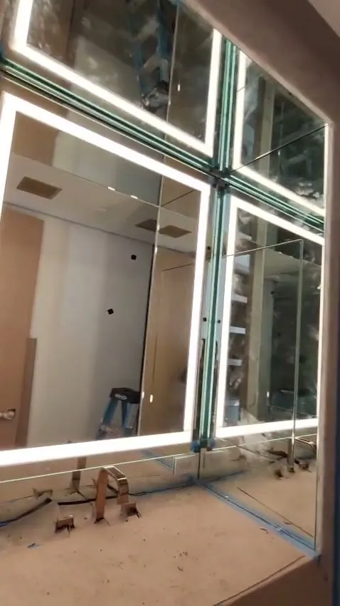Custom backlit LED vanity mirrors wrapping a corner during installation in a Los Angeles primary bathroom