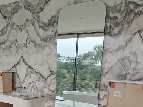 Full-height rounded-top mirror over a marble vanity in a Los Angeles bathroom