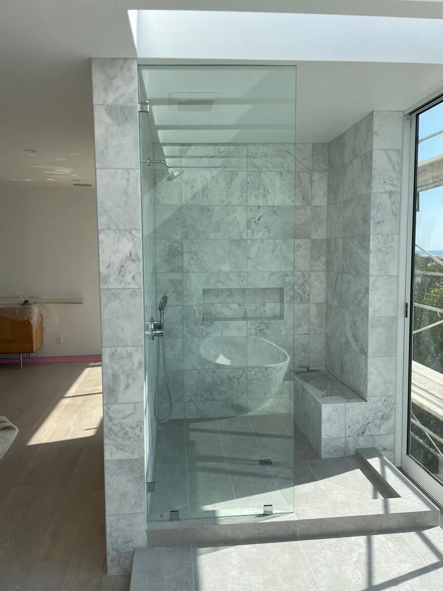 Finished frameless glass shower enclosure with marble tile, built-in bench, and skylight in a Los Angeles primary bathroom