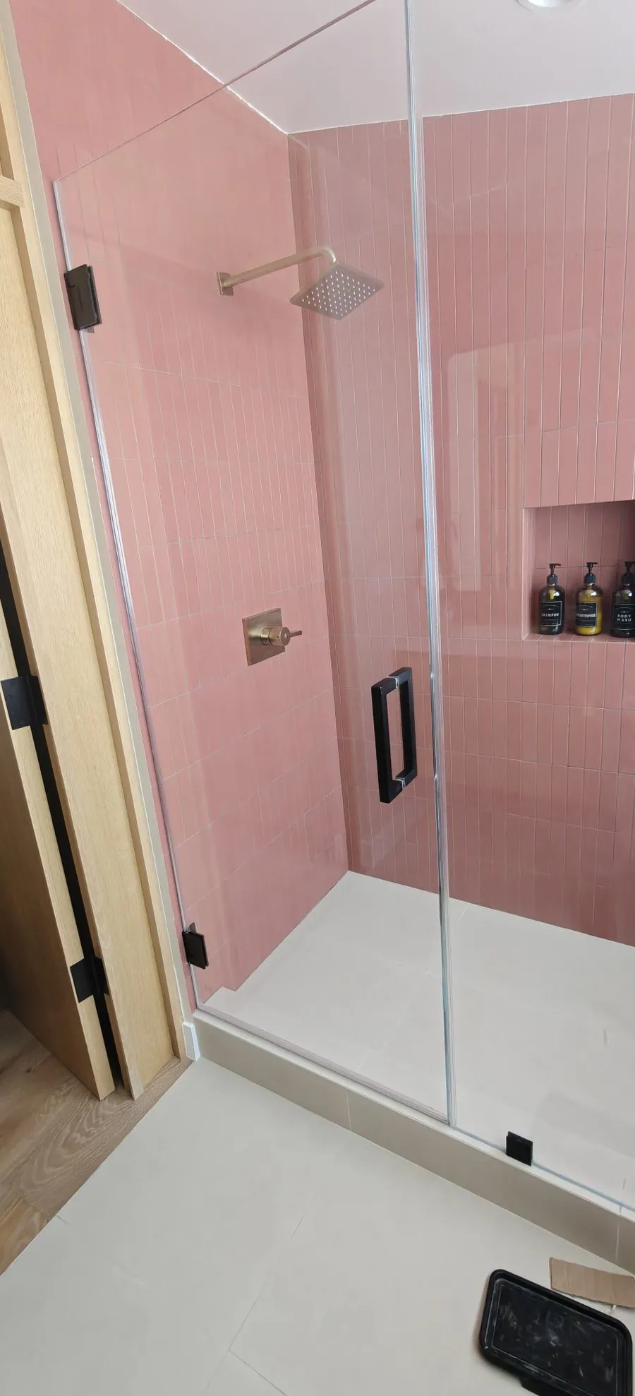 Finished frameless shower enclosure with pink vertical tile, brass fixtures, and black pull handle in Los Angeles