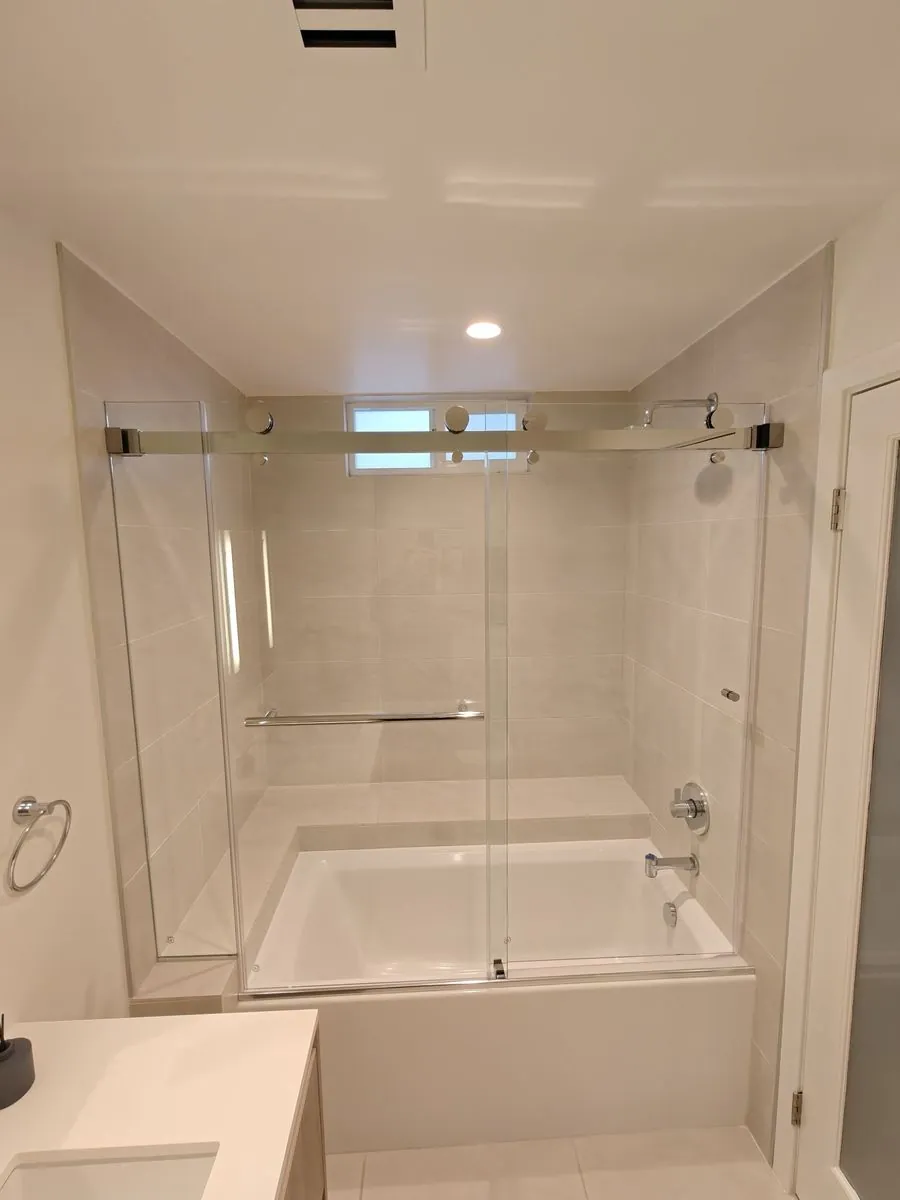 Frameless sliding shower door on a chrome roller track over a tub, installed by Versa Glass Co. in Los Angeles