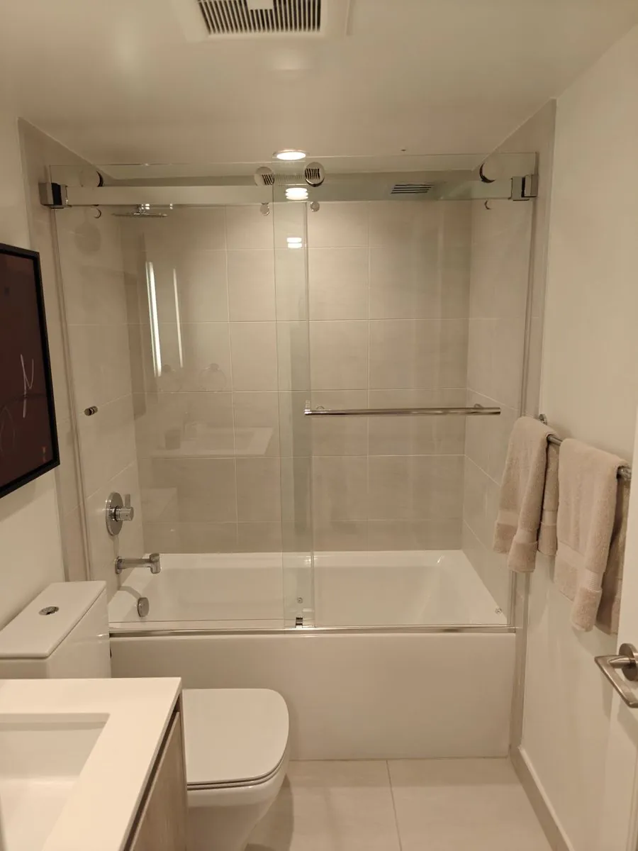 Frameless sliding glass tub enclosure with chrome roller track and towel bar handle in a Los Angeles bathroom