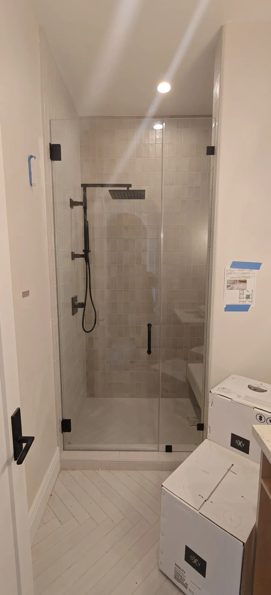 Completed frameless shower enclosure with matte black hardware, tiled bench, and herringbone floor in a Los Angeles home